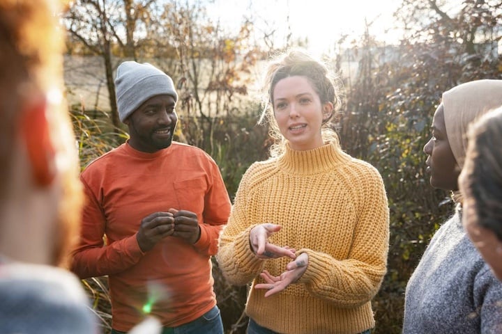 Diverse group of adults standing outside together actively talking, interacting and smiling.