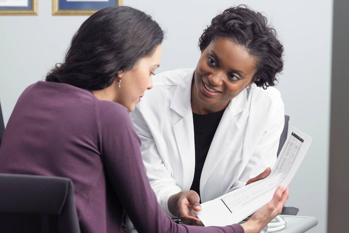 A practitioner seated with a patient, talking and reviewing a medical document together.